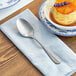 An Acopa Josette stainless steel dinner spoon on a napkin next to a plate of food.