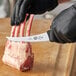 A person in black gloves using a Victorinox curved boning knife to cut meat.