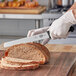 A person using a Victorinox wavy edge slicing knife to cut bread on a wooden cutting board.