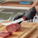 A person using a Victorinox Breaking Knife to cut meat on a cutting board.