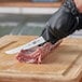 A person in black gloves using a Victorinox curved boning knife to cut meat on a cutting board.