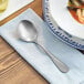 An Acopa Josette stainless steel bouillon spoon on a napkin next to a bowl of soup.