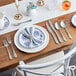 A table set with white and blue plates, Acopa Josette bouillon spoons, and silverware.