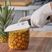 A person using a Victorinox Santoku knife to cut a pineapple on a counter.