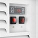 A control panel with a digital temperature display and two red rocker switches on a white refrigerated air curtain merchandiser.