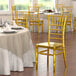 A gold Lancaster Table & Seating Chiavari chair next to a table with a white tablecloth and a plate.