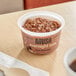 A bowl of chocolate oatmeal on a table with a spoon and a cup of coffee.