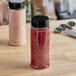 Two 12 oz. round plastic spice containers with red grains on a counter.