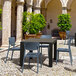 A Siesta Monna dark gray resin outdoor dining chair and table on a stone surface.