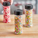 Three round plastic spice containers with colorful sprinkles on top.