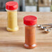 Two 7 oz. round plastic spice containers with dual flapper lids holding spices on a table.