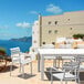 A white Siesta Paris resin outdoor dining arm chair on a table on an outdoor patio overlooking the ocean.