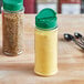 Two round plastic spice containers with green lids on a table with black spoons.
