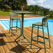 A Siesta Sky olive green bar height foldable table on an outdoor patio next to a pool.