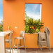 A stack of Siesta Maya taupe outdoor restaurant bar stools on a table on an outdoor patio.