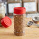A round plastic spice container with a red flip and sift lid on a table.