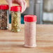 A hand holding a round plastic spice container filled with spices on a home kitchen counter.