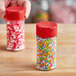 Two 3.5 oz. round plastic spice containers with red flip and sift lids filled with colorful sprinkles.