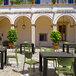 A Siesta Monna olive green resin outdoor dining chair on a stone courtyard next to a table.