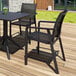 A Siesta Pacific black resin outdoor arm chair with black sling on a deck with a table and vase of flowers.
