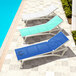 A row of Siesta Pacific white resin outdoor chaise lounges with blue slings next to a pool.