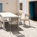 A taupe Siesta Helen resin dining chair on an outdoor patio with a table.