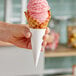 A hand holding a Joy white paper waffle cone with a scoop of pink ice cream.