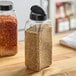 A clear plastic rectangular spice container with a black dual flapper lid filled with spices.