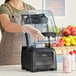 A woman in an apron using a Vitamix Quick and Quiet blender to make a smoothie.