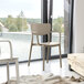 A Siesta Lisa taupe resin outdoor dining arm chair in front of a window.