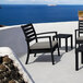 A Siesta Artemis XL black outdoor club arm chair with a taupe cushion on a patio overlooking the ocean.