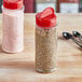 Two round plastic spice containers with red lids and spoons on a kitchen counter.