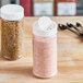 Two 16 oz. round plastic spice containers with white lids filled with seasoning on a wooden table.