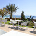 A Siesta Sky white plastic table on a patio with white chairs overlooking the beach.