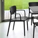 A black Siesta Lisa resin outdoor dining arm chair on a table in an outdoor patio.