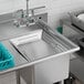 A Regency stainless steel pre-rinse basket with handles in a blue tray above a stainless steel sink.