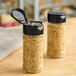 Two 4 oz. round plastic spice containers with black flip and sift lids filled with seasoning.