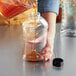 A person pouring honey into a ribbed plastic honey bottle on a kitchen counter.