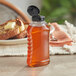 An 11 oz. ribbed hourglass PET honey bottle with black flip top lid filled with liquid on a table.
