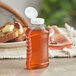 A 11 oz. Ribbed Hourglass PET Honey Bottle with a white plastic flip top lid filled with honey on a table.