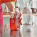 A person pouring honey from a brown bottle into a jar.