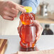 A person holding a 16 oz. honey bear jar with a yellow flip top lid.