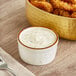 A bowl of fried food with a bowl of Ken's Tartar Sauce on a table with a fork.