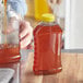 A person pouring honey into a Ribbed Hourglass PET Honey Bottle on a table.