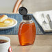A Queenline PET honey bottle filled with honey and topped with a black flip top lid on a table.