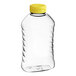 A clear plastic ribbed hourglass honey bottle with a yellow flip top lid.