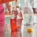 A person pouring honey into a yellow bottle with a flip top lid.