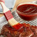 A person using a brush to spread Sweet Baby Ray's Original BBQ Sauce on a steak.