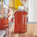 A person pouring honey into a ribbed hourglass PET honey bottle.