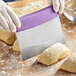 A person using a Choice stainless steel dough cutter with a purple handle to cut dough.